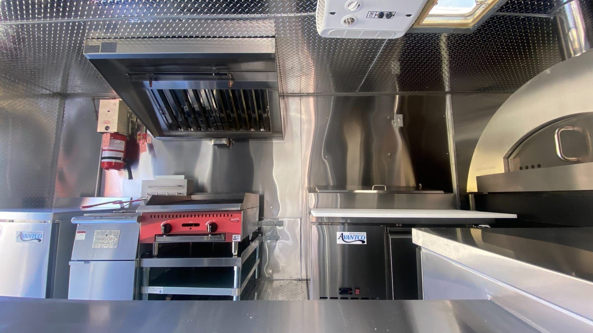 Wide view of the pizza truck kitchen: hood, griddle, refrigerated prep and oven