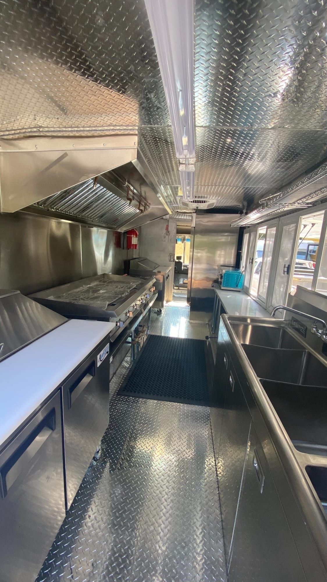 Cocina de acero inoxidable con plancha, mesas de preparación y ventanas de servicio en el truck de Tacos Los Primos
